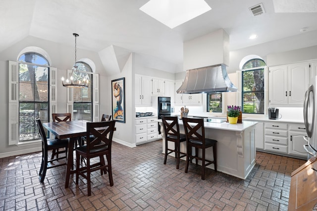 interior space with visible vents, baseboards, lofted ceiling with skylight, brick floor, and a chandelier