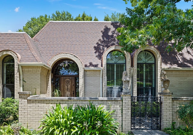 view of front of house with a shingled roof, a gate, and brick siding