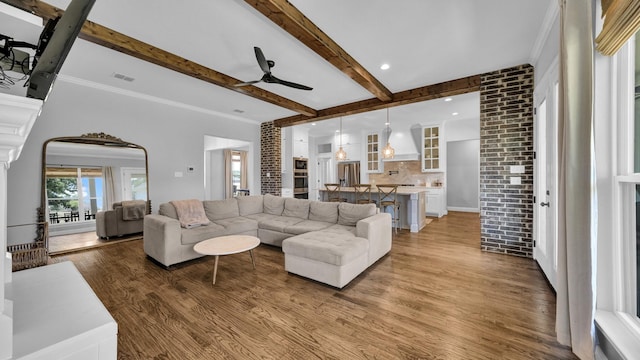 living room featuring a ceiling fan, visible vents, beamed ceiling, and wood finished floors