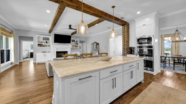 kitchen with a kitchen island, open floor plan, a fireplace, white cabinetry, and pendant lighting