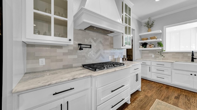 kitchen with light stone counters, white cabinets, custom exhaust hood, glass insert cabinets, and crown molding