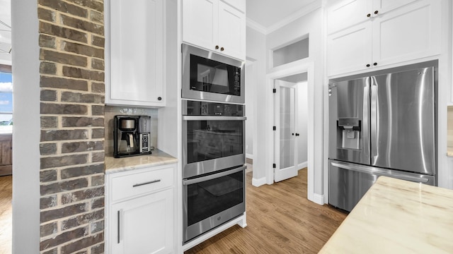 kitchen with wood finished floors, white cabinetry, ornamental molding, appliances with stainless steel finishes, and light stone countertops