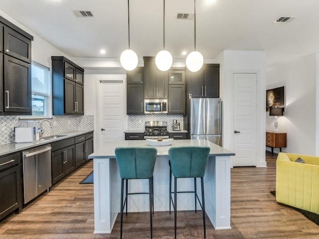 kitchen with glass insert cabinets, a kitchen island, appliances with stainless steel finishes, and hanging light fixtures