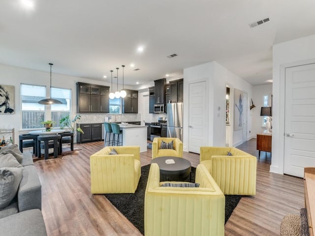 living room featuring baseboards, light wood-type flooring, visible vents, and recessed lighting