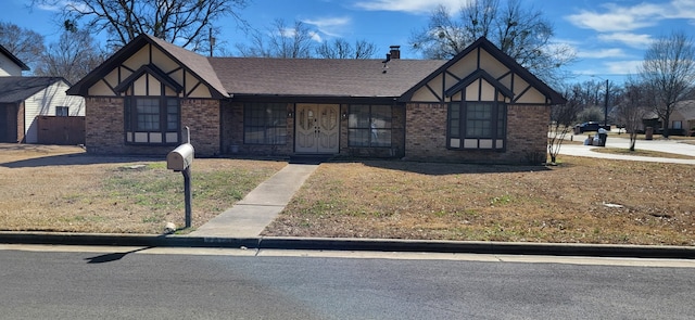 english style home with roof with shingles, a chimney, a front lawn, and brick siding