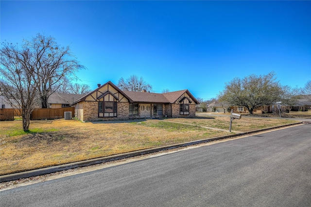 tudor home featuring brick siding, central air condition unit, a front lawn, and fence