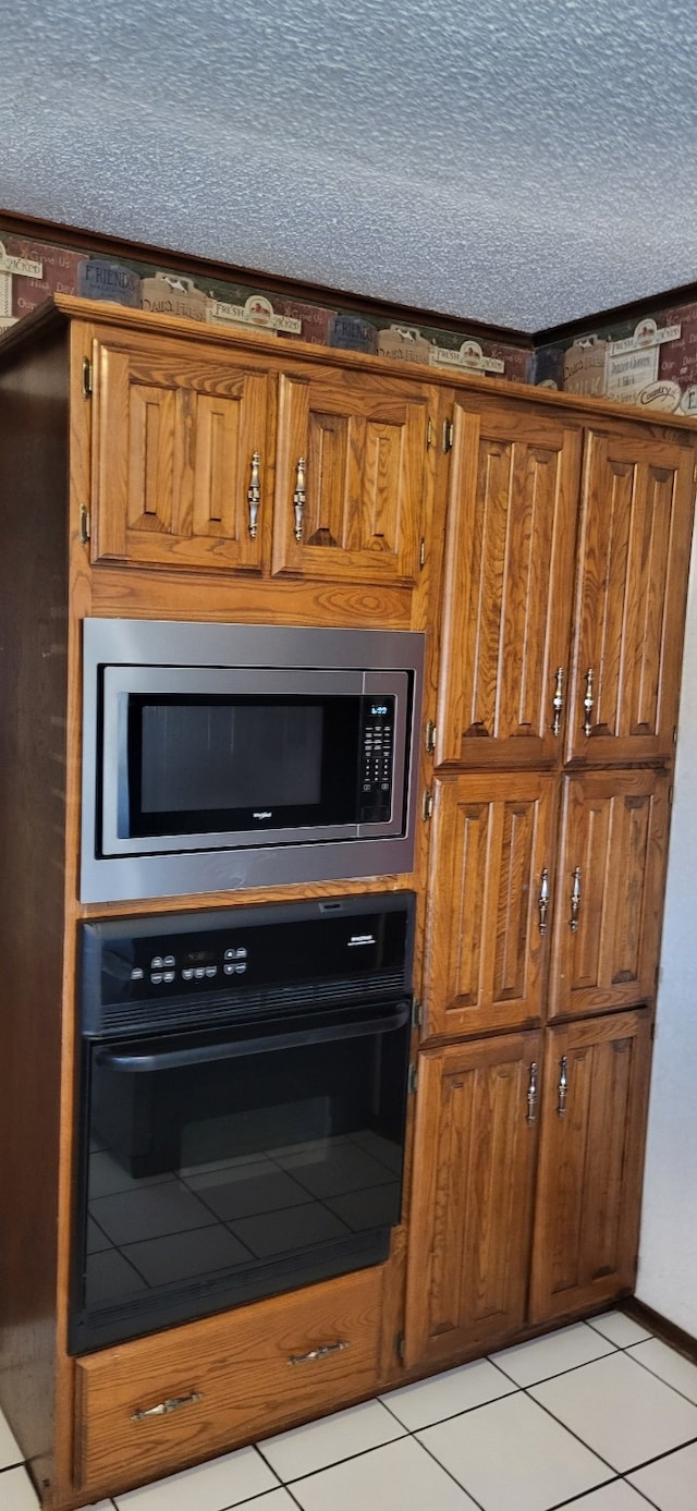 kitchen featuring a textured ceiling, black oven, stainless steel microwave, and brown cabinetry