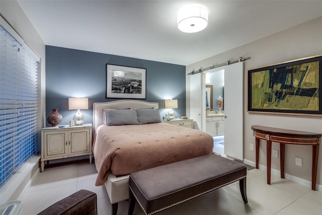 bedroom with light tile patterned floors, a barn door, baseboards, and ensuite bathroom