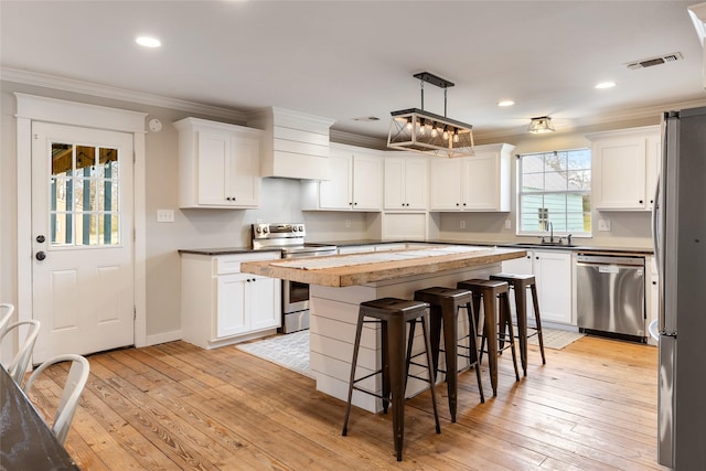 kitchen featuring crown molding, stainless steel appliances, a center island, and white cabinets