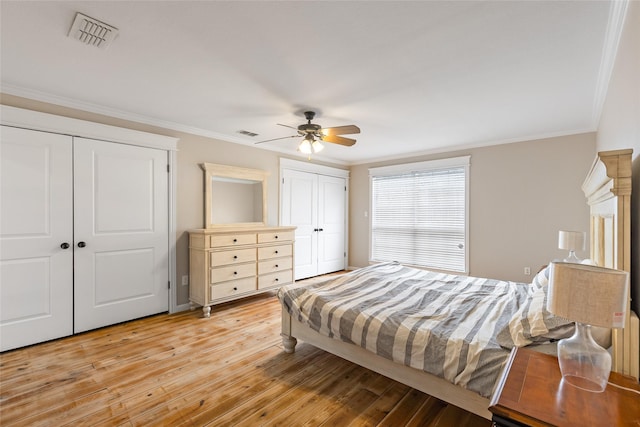 bedroom with light wood-style floors, visible vents, multiple closets, and ornamental molding