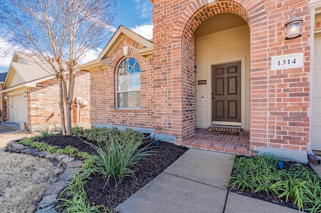 view of exterior entry featuring a garage and brick siding