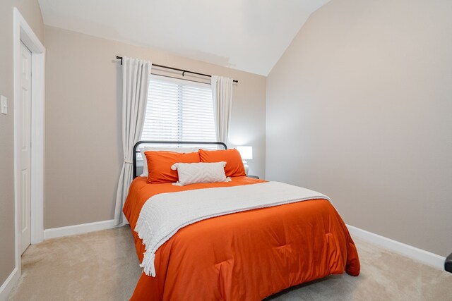 bedroom with light carpet, lofted ceiling, and baseboards