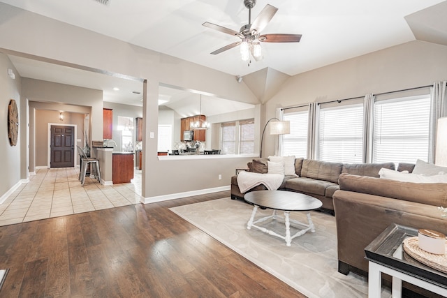 living area featuring light wood finished floors, baseboards, vaulted ceiling, and a ceiling fan