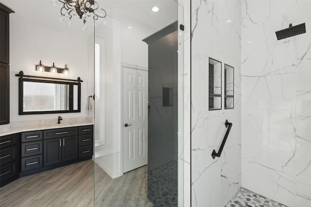 bathroom featuring vanity, wood finished floors, recessed lighting, a marble finish shower, and a notable chandelier