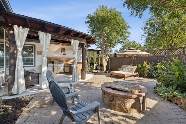 view of patio featuring an outdoor kitchen, ceiling fan, a fire pit, and a fenced backyard