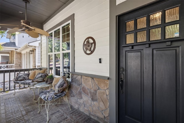 property entrance featuring covered porch, a ceiling fan, and stone siding