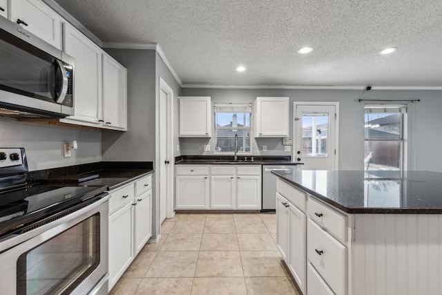 kitchen with light tile patterned floors, stainless steel appliances, white cabinetry, a sink, and dark stone counters