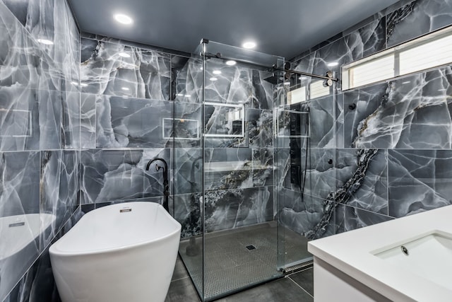 bathroom with a freestanding bath, a marble finish shower, tile walls, and vanity