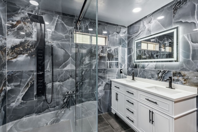 bathroom featuring a marble finish shower, double vanity, a sink, and tile walls