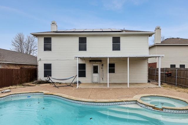 rear view of house featuring a fenced backyard, solar panels, a pool with connected hot tub, a chimney, and a patio area