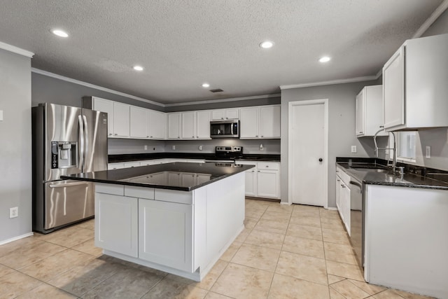 kitchen with dark countertops, appliances with stainless steel finishes, white cabinetry, a kitchen island, and a sink