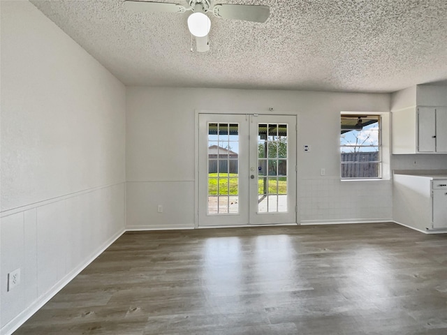 unfurnished dining area with wainscoting, dark wood finished floors, a textured ceiling, and french doors