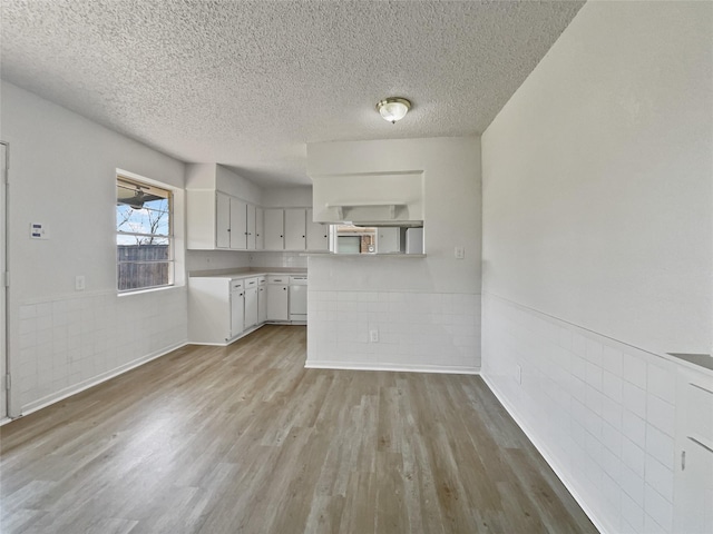 kitchen featuring light wood finished floors, a wainscoted wall, light countertops, a textured ceiling, and white cabinetry