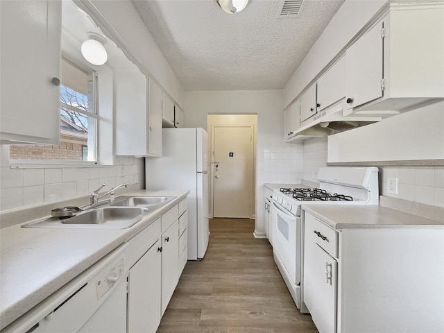 kitchen with white appliances, white cabinets, light countertops, under cabinet range hood, and a sink