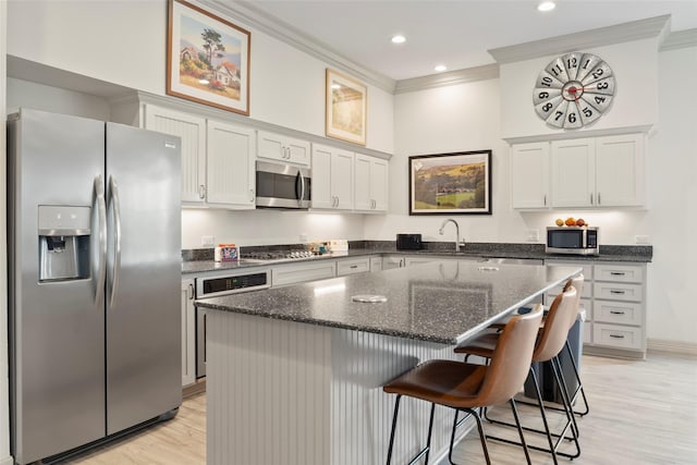 kitchen featuring stainless steel appliances, a center island, dark stone counters, a kitchen bar, and crown molding