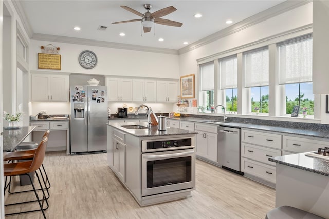 kitchen with stainless steel appliances, white cabinets, a kitchen island with sink, and ornamental molding