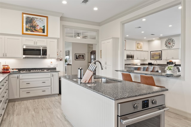 kitchen with stainless steel appliances, a sink, white cabinetry, dark stone counters, and an island with sink