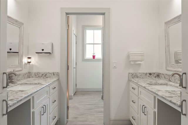 bathroom featuring two vanities, a sink, baseboards, and wood finished floors