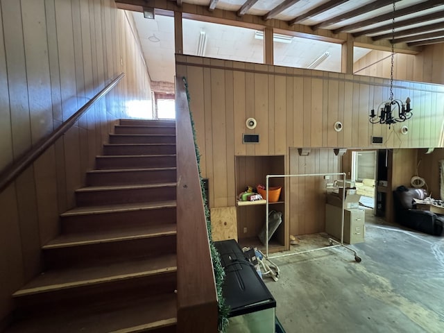 stairs featuring a chandelier, unfinished concrete flooring, beam ceiling, and wood walls