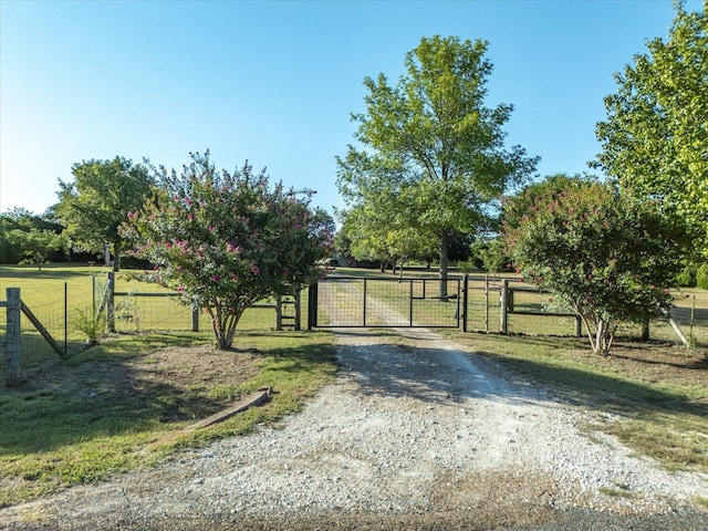 view of gate with a yard, a rural view, and fence