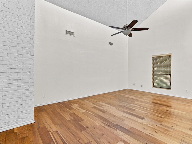 spare room featuring visible vents, a ceiling fan, a high ceiling, a textured ceiling, and light wood-style floors