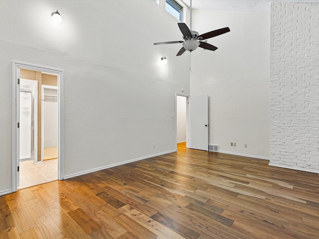 empty room with visible vents, ceiling fan, wood finished floors, high vaulted ceiling, and baseboards