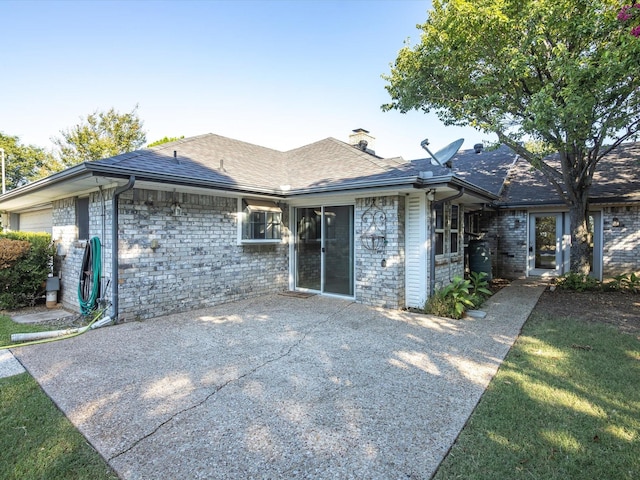 ranch-style home featuring a patio area, a chimney, brick siding, and roof with shingles