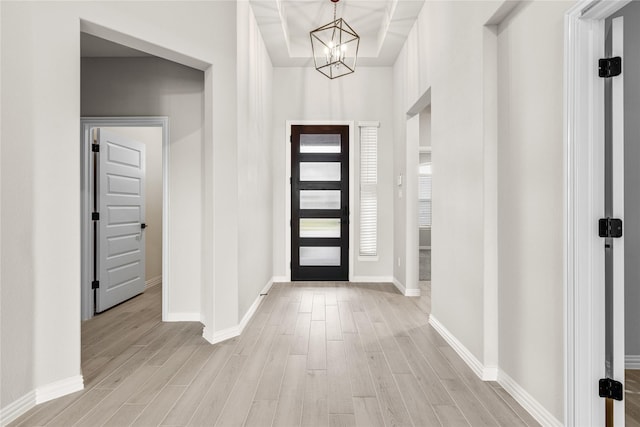 entryway featuring light wood-type flooring, a raised ceiling, baseboards, and an inviting chandelier