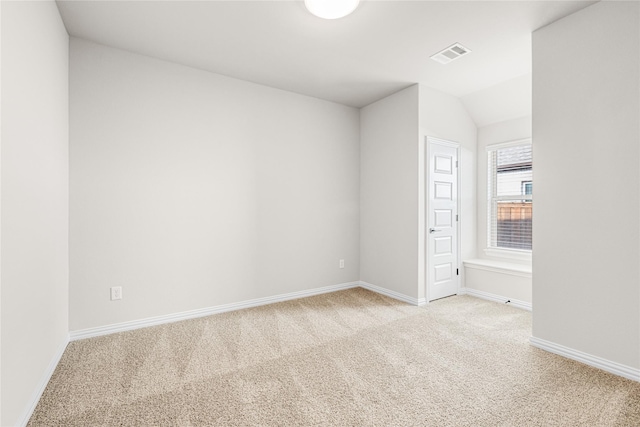 spare room with light colored carpet, visible vents, vaulted ceiling, and baseboards