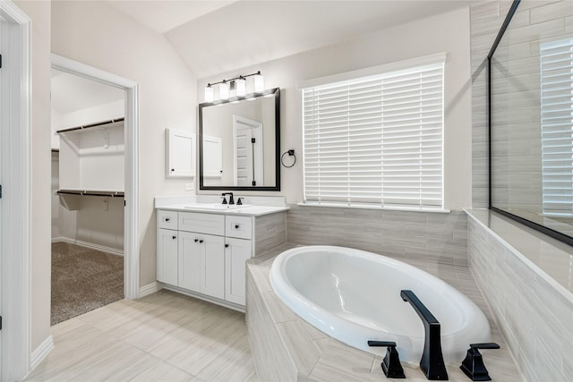 full bath featuring baseboards, a garden tub, a spacious closet, vaulted ceiling, and vanity