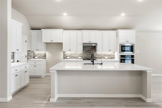 kitchen featuring under cabinet range hood, a center island with sink, stainless steel oven, and light countertops