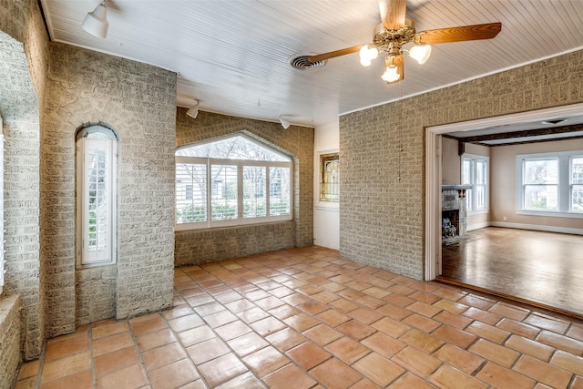 empty room with light tile patterned flooring, brick wall, a fireplace, visible vents, and a ceiling fan