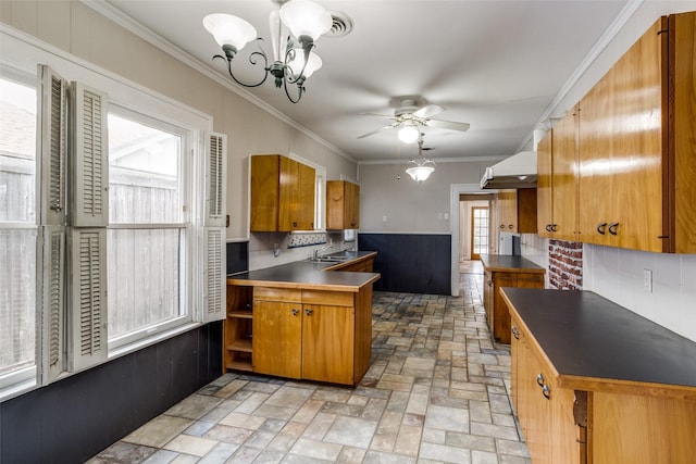 kitchen featuring ceiling fan with notable chandelier, ornamental molding, tasteful backsplash, brown cabinetry, and dark countertops