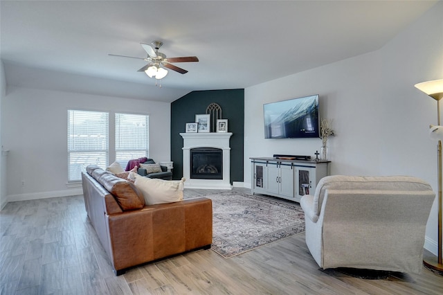 living area with a ceiling fan, baseboards, vaulted ceiling, light wood finished floors, and a glass covered fireplace