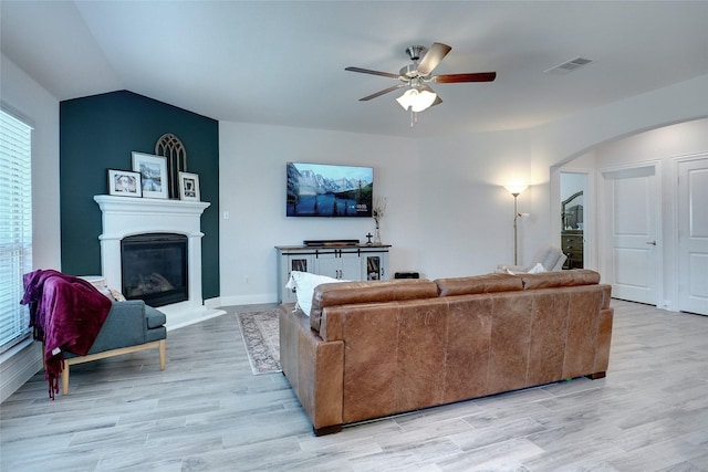 living room featuring light wood-style floors, visible vents, arched walkways, and a glass covered fireplace