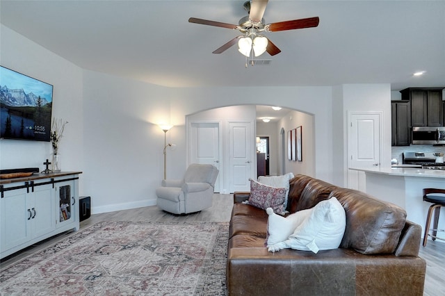 living area featuring arched walkways, visible vents, baseboards, a ceiling fan, and light wood-style floors