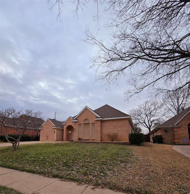 view of front facade with brick siding, a front lawn, and roof with shingles