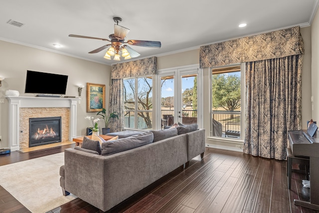 living room with visible vents, dark wood-type flooring, a glass covered fireplace, ornamental molding, and a ceiling fan