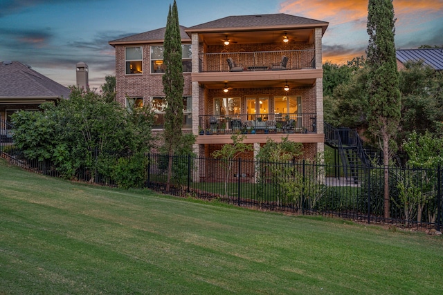 rear view of house with brick siding, a lawn, fence, ceiling fan, and a balcony