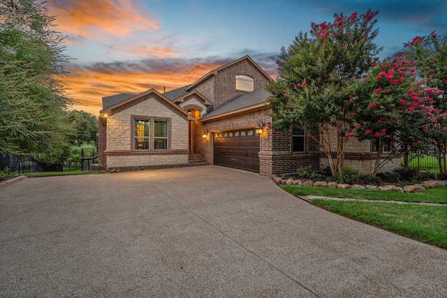 french country home with concrete driveway, stone siding, an attached garage, fence, and brick siding